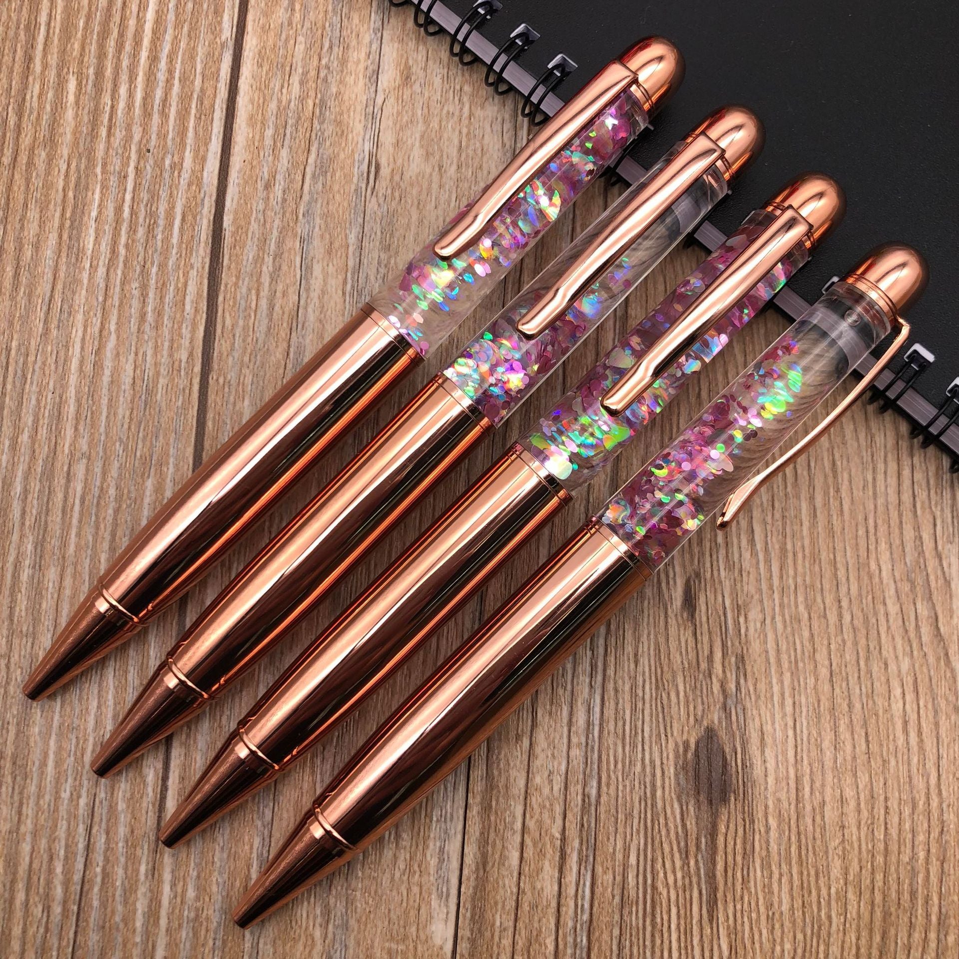 Stationery Large Fat Rose Gold Liquid Ball Pen collection with glitter accents on a wooden desk.
