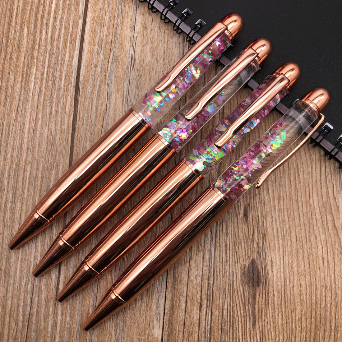 Stationery Large Fat Rose Gold Liquid Ball Pen collection with glitter accents on a wooden desk.