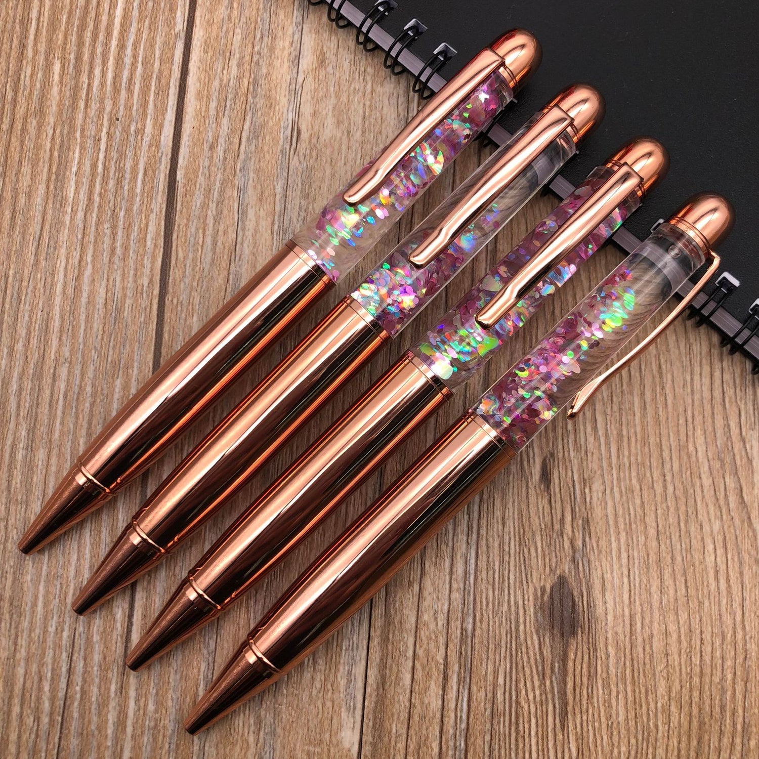 Stationery Large Fat Rose Gold Liquid Ball Pen collection with glitter accents on a wooden desk.